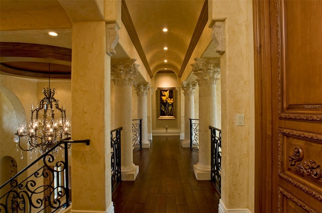 corridor with crown molding, dark hardwood / wood-style floors, an inviting chandelier, ornate columns, and lofted ceiling