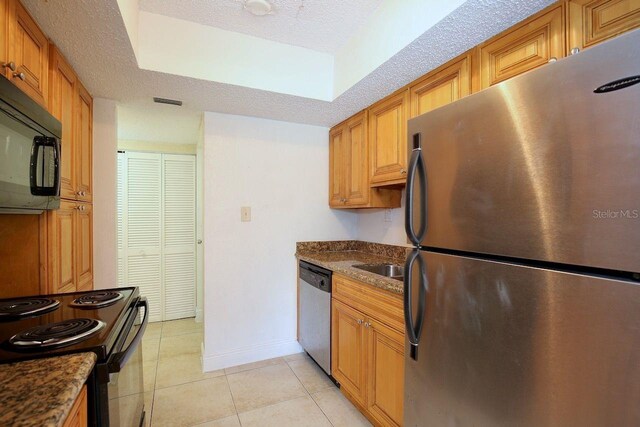 kitchen featuring light tile floors, a textured ceiling, a raised ceiling, stainless steel appliances, and dark stone countertops