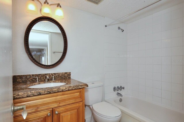 full bathroom featuring tiled shower / bath combo, a textured ceiling, large vanity, and toilet