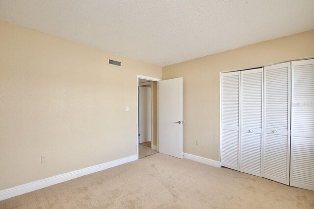 unfurnished bedroom with light carpet, a closet, and a textured ceiling