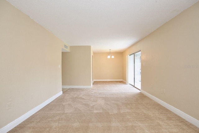 empty room featuring a notable chandelier, carpet floors, and a textured ceiling