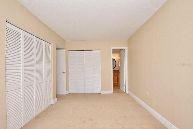 unfurnished bedroom featuring ensuite bath, light colored carpet, and a textured ceiling