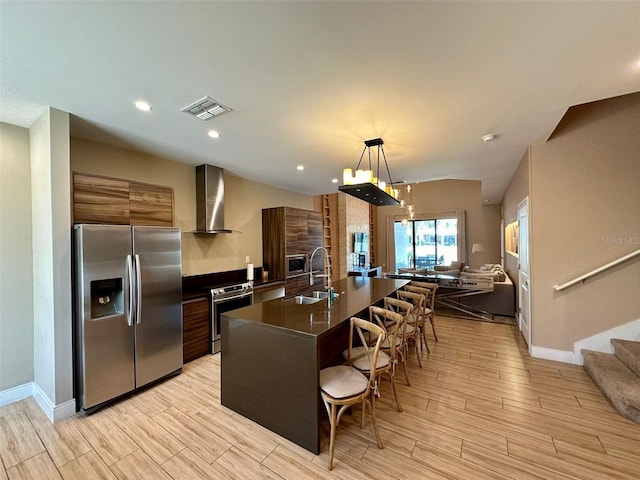 kitchen with an island with sink, stainless steel appliances, a kitchen breakfast bar, sink, and wall chimney exhaust hood