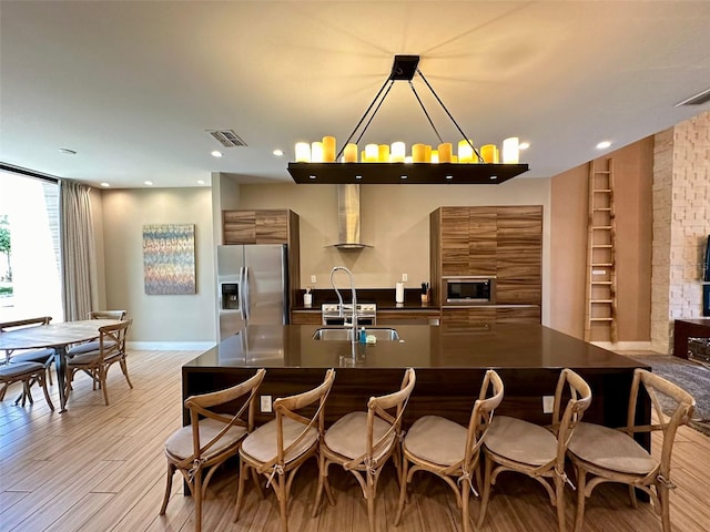 kitchen featuring light hardwood / wood-style floors, stainless steel appliances, sink, wall chimney range hood, and hanging light fixtures