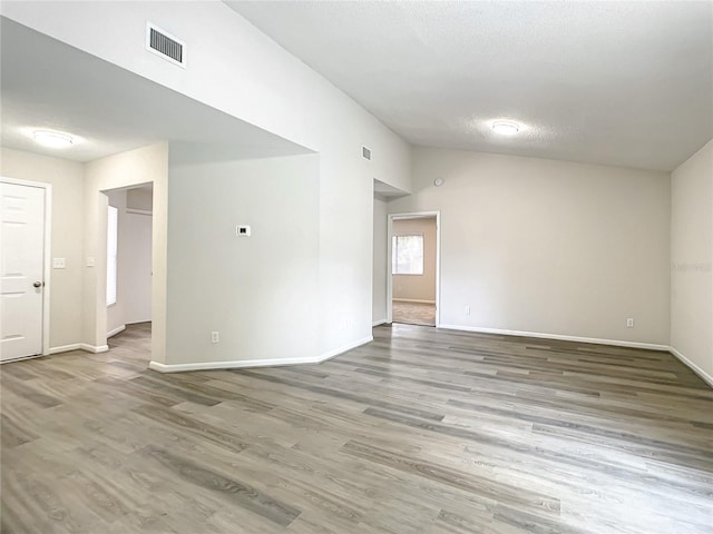 spare room featuring lofted ceiling, a textured ceiling, wood finished floors, and visible vents