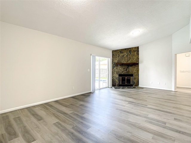 unfurnished living room with light wood-style flooring, baseboards, a textured ceiling, and a stone fireplace