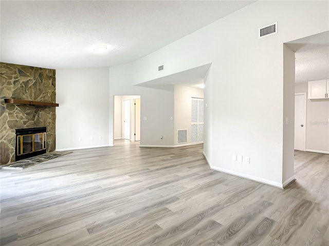 unfurnished living room with visible vents, lofted ceiling, a textured ceiling, light wood-style floors, and a fireplace