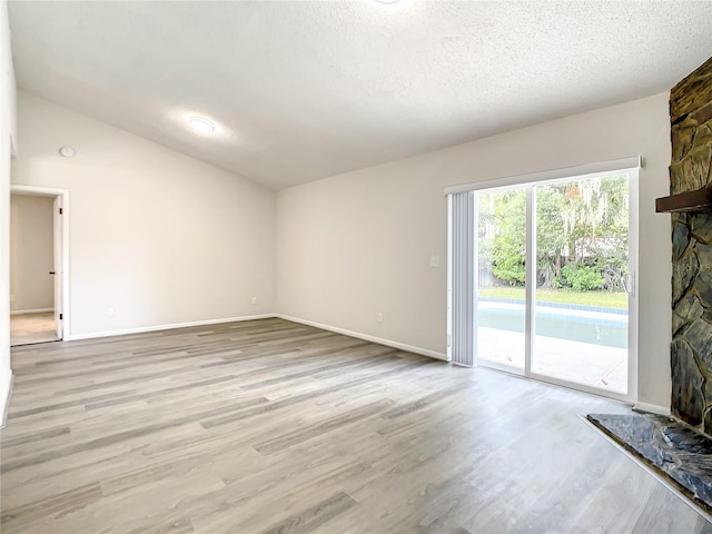 unfurnished living room with lofted ceiling, a textured ceiling, a stone fireplace, baseboards, and light wood finished floors