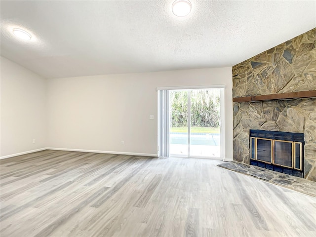 unfurnished living room featuring a textured ceiling, a stone fireplace, wood finished floors, and baseboards