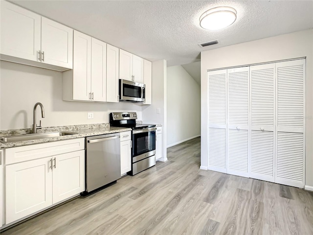 kitchen with stainless steel appliances, light wood-type flooring, white cabinetry, and a sink