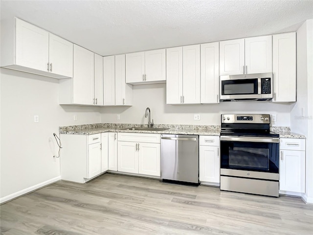 kitchen featuring a textured ceiling, appliances with stainless steel finishes, a sink, and white cabinetry