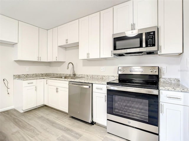 kitchen with a sink, white cabinets, appliances with stainless steel finishes, light wood-type flooring, and light stone countertops