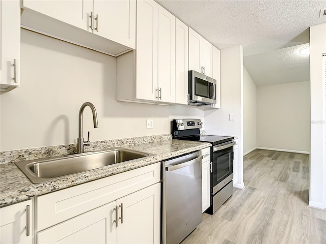 kitchen featuring appliances with stainless steel finishes, white cabinets, a textured ceiling, and light stone countertops