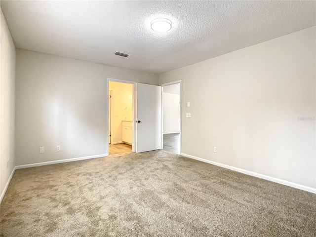 unfurnished bedroom with baseboards, visible vents, connected bathroom, a textured ceiling, and carpet flooring