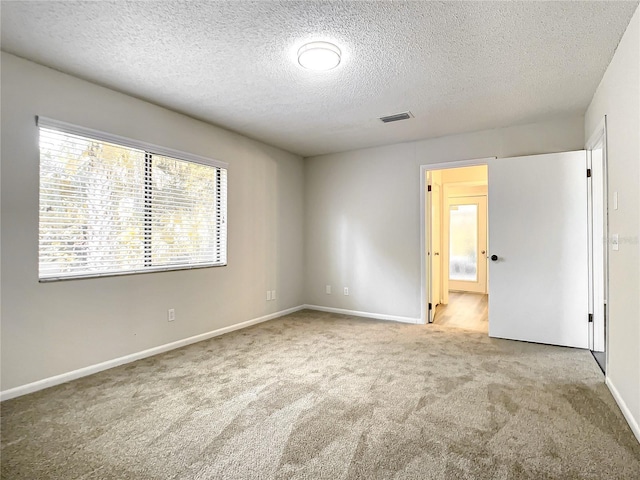 spare room with light colored carpet, visible vents, a textured ceiling, and baseboards