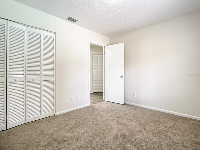 unfurnished bedroom featuring a closet, light colored carpet, visible vents, a textured ceiling, and baseboards