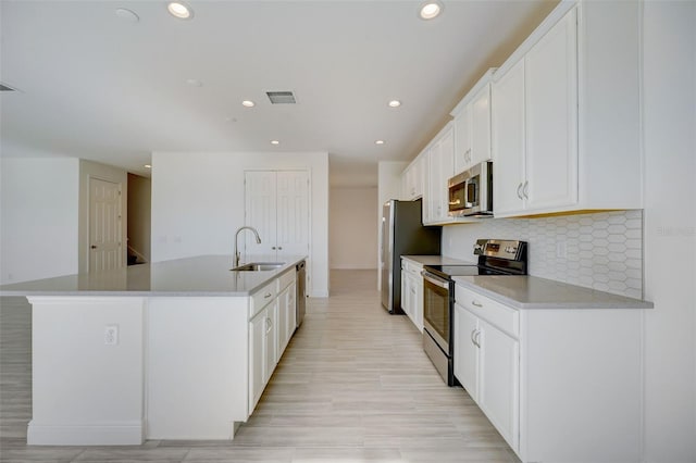 kitchen featuring stainless steel appliances, a center island with sink, tasteful backsplash, white cabinetry, and sink