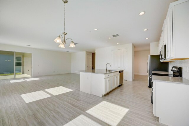 kitchen featuring decorative light fixtures, stainless steel appliances, an island with sink, white cabinets, and sink