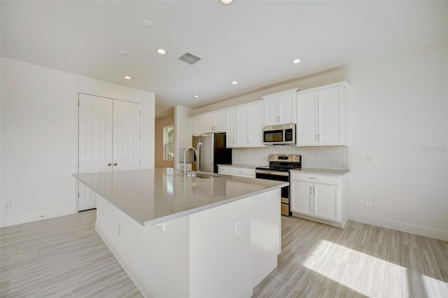 kitchen with backsplash, stainless steel appliances, white cabinetry, and a kitchen island with sink