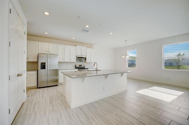 kitchen with tasteful backsplash, stainless steel appliances, white cabinetry, and an island with sink