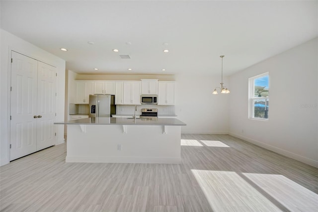 kitchen with backsplash, stainless steel appliances, white cabinetry, and an island with sink