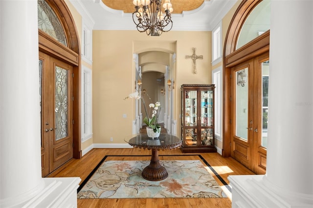 foyer featuring crown molding, light hardwood / wood-style floors, decorative columns, and a notable chandelier