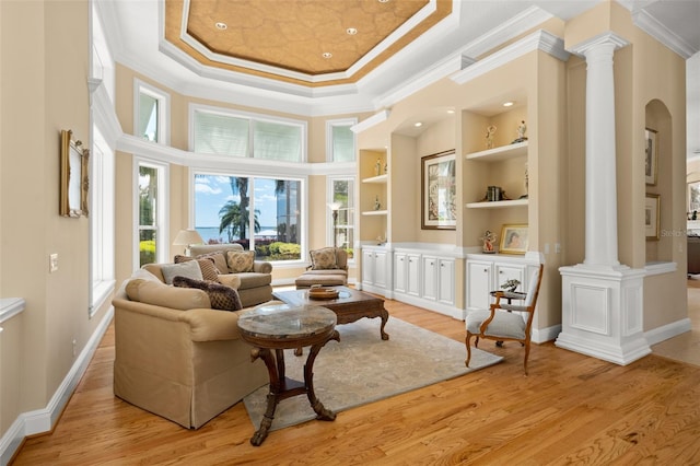 sitting room featuring a towering ceiling, light hardwood / wood-style floors, a tray ceiling, ornamental molding, and ornate columns