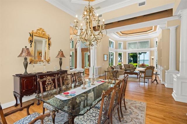 dining area featuring crown molding, ornate columns, a raised ceiling, and light wood-type flooring