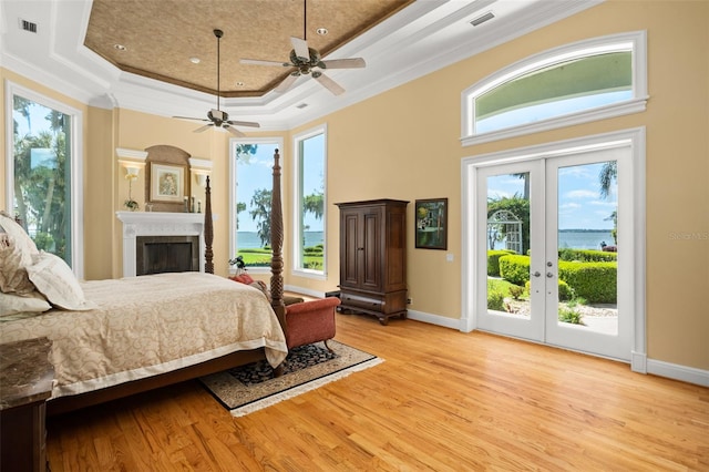 bedroom featuring light hardwood / wood-style floors, french doors, a raised ceiling, and access to exterior