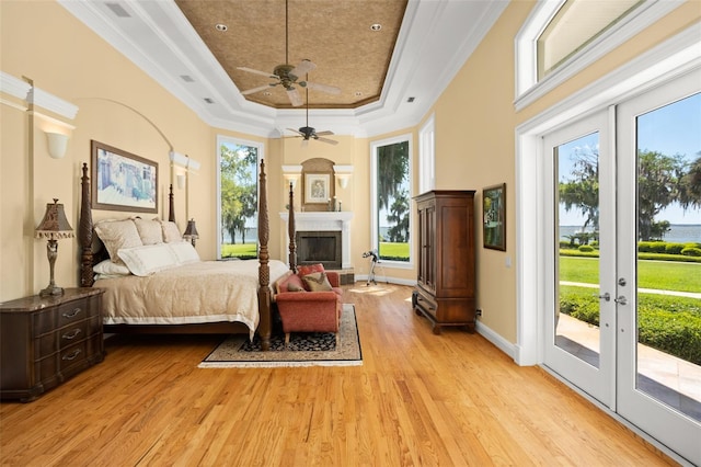 bedroom with light hardwood / wood-style flooring, ornamental molding, a tray ceiling, and multiple windows