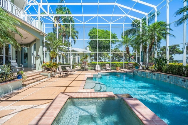 view of pool featuring glass enclosure, an in ground hot tub, and a patio area