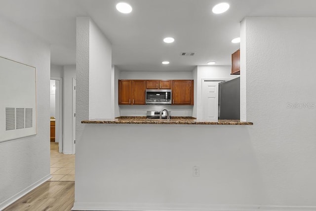 kitchen featuring sink, refrigerator, light tile floors, and dark stone counters