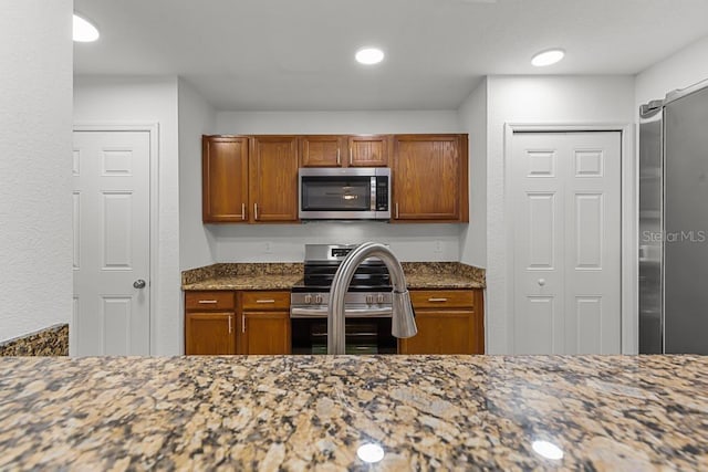 kitchen with appliances with stainless steel finishes, dark stone countertops, and sink