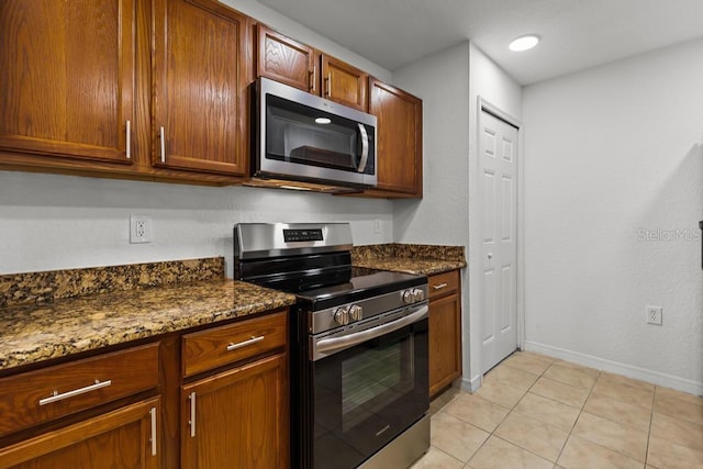 kitchen with dark stone countertops, stainless steel appliances, and light tile flooring