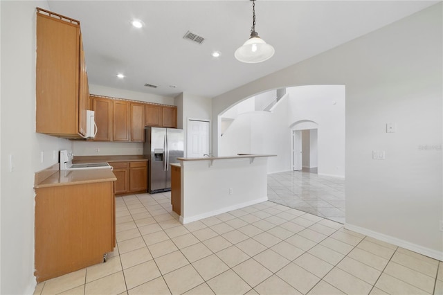 kitchen with stove, light tile floors, a center island, pendant lighting, and stainless steel fridge