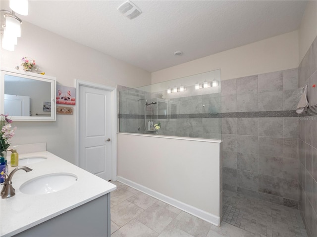 bathroom with a shower with shower door, double vanity, tile flooring, and a textured ceiling