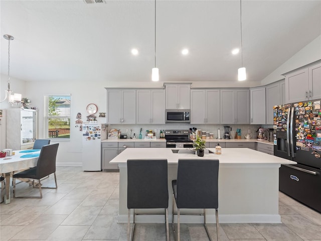 kitchen featuring a breakfast bar, gray cabinetry, decorative light fixtures, stainless steel appliances, and a center island with sink