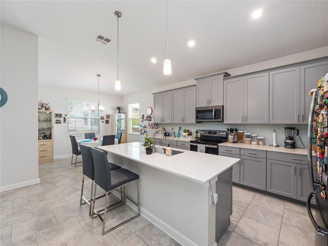 kitchen with a kitchen island with sink, gray cabinetry, pendant lighting, and stainless steel appliances