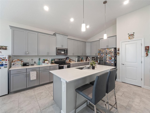 kitchen featuring decorative light fixtures, appliances with stainless steel finishes, gray cabinets, a kitchen island with sink, and sink