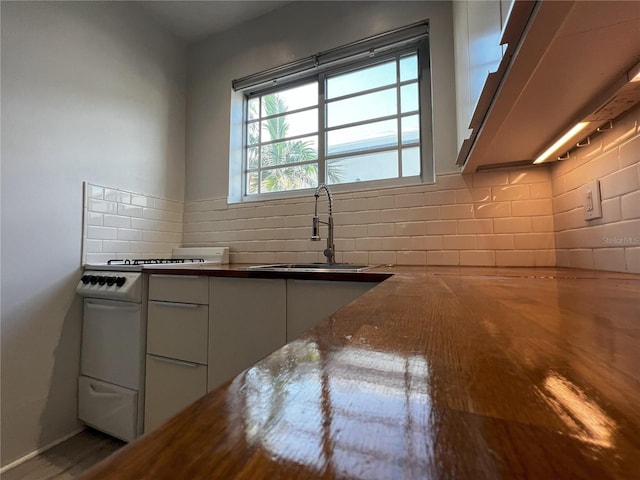 kitchen with white cabinetry, tasteful backsplash, white range oven, and sink