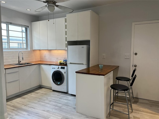 kitchen with white refrigerator, washer / clothes dryer, white cabinetry, sink, and light hardwood / wood-style floors