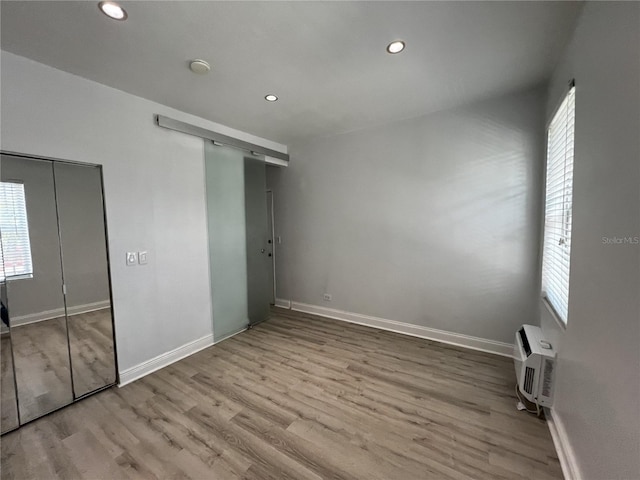 unfurnished bedroom with an AC wall unit and light hardwood / wood-style flooring