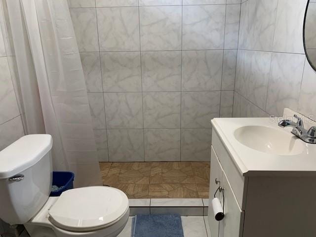 bathroom featuring tile flooring, vanity, toilet, and tile walls