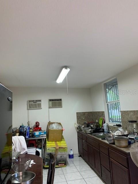 kitchen with a wall unit AC, dark brown cabinets, sink, and light tile flooring