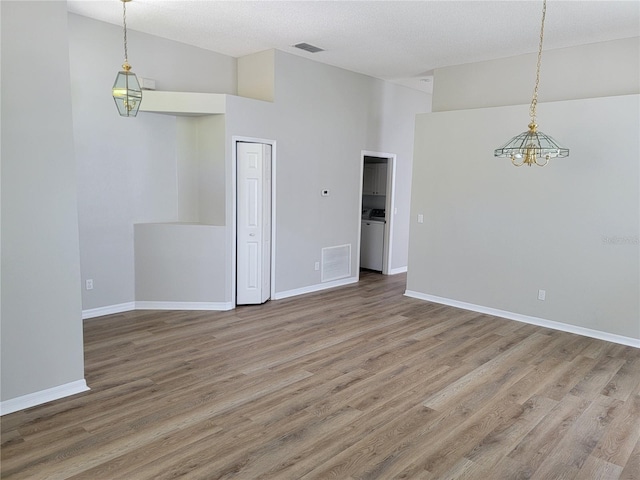 spare room with a textured ceiling, hardwood / wood-style flooring, an inviting chandelier, a high ceiling, and washer / dryer