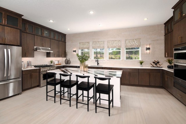 kitchen with a kitchen island, a kitchen bar, stainless steel appliances, sink, and dark brown cabinets