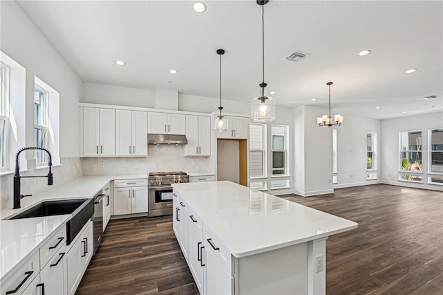 kitchen featuring white cabinetry, stainless steel appliances, decorative light fixtures, light stone countertops, and a center island