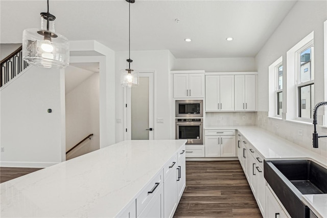 kitchen featuring white cabinetry, stainless steel appliances, light stone countertops, pendant lighting, and sink