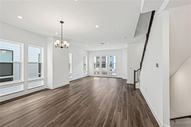 unfurnished living room featuring an inviting chandelier and dark hardwood / wood-style flooring