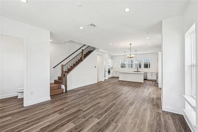 unfurnished living room featuring an inviting chandelier, dark hardwood / wood-style floors, and sink